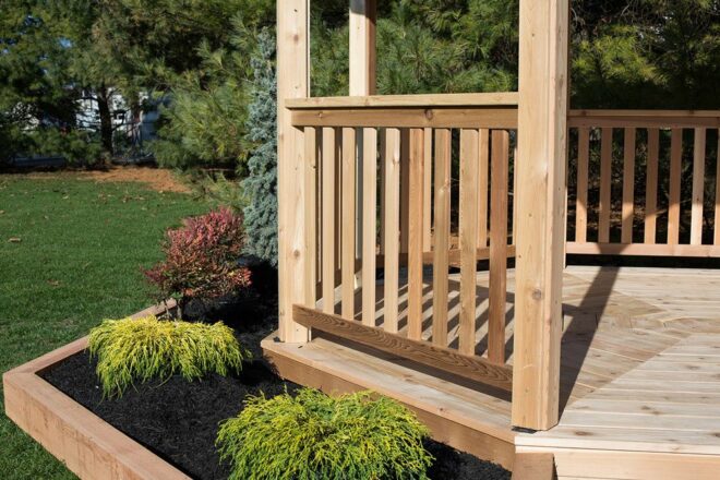 A wood gazebo handrail with an adjoined flower garden row.